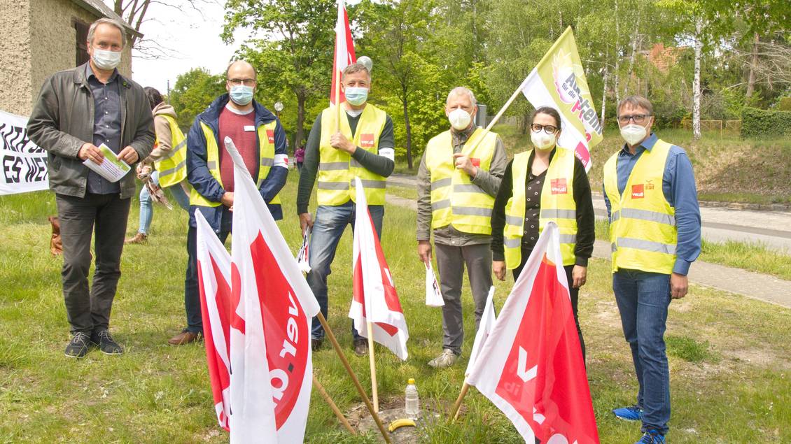 Mehrere Menschen mit Warnwesten und Mund-Nase-Bedeckung, die Fahnen mit Verdi-Logo tragen