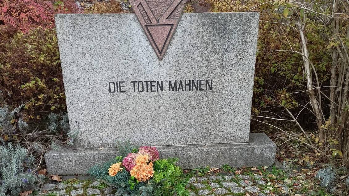 Das Foto zeigt einen Gedenkstein mit der Aufschrift "Die Toten mahnen", davor befindet sich ein Blumengebinde.