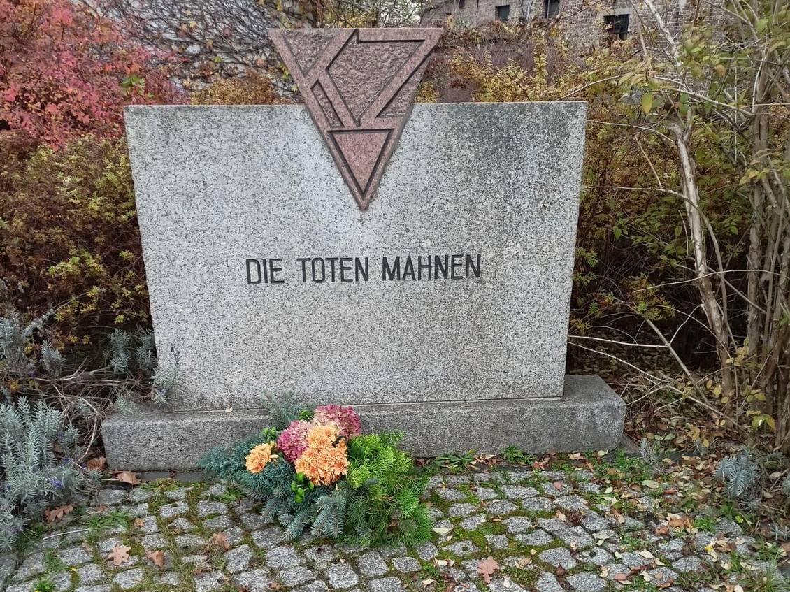 Das Foto zeigt einen Gedenkstein mit der Aufschrift "Die Toten mahnen", davor befindet sich ein Blumengebinde.
