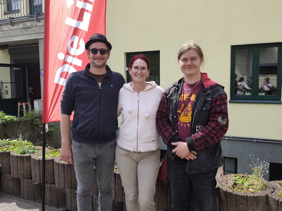 Das Foto zeigt drei Personen vor einem Haus, neben ihnen weht eine Fahne der Partei Die Linke.