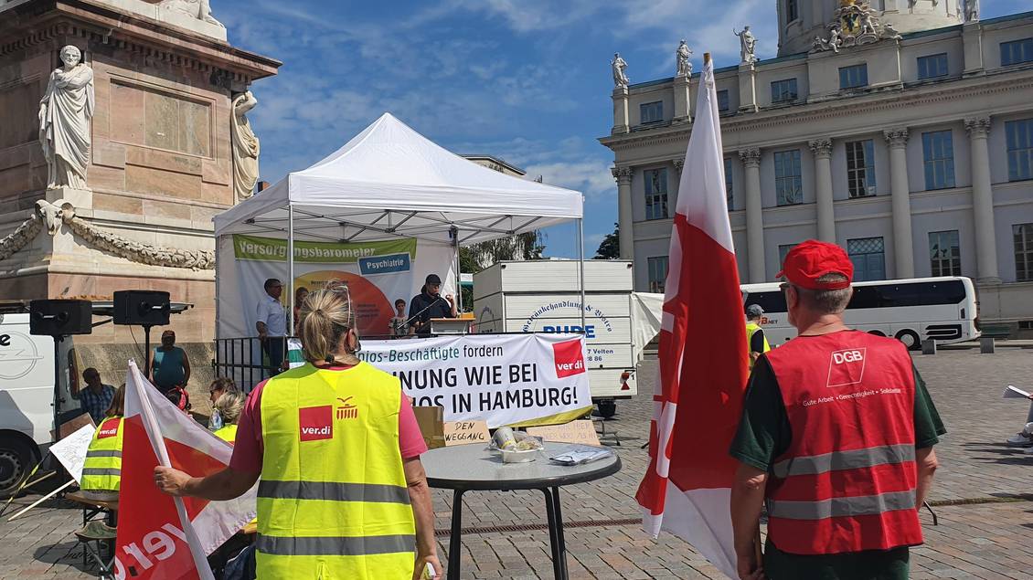 Menschen mit Warnwesten und Fahnen mit Logos der Gewerkschaften stehen vor dem Potsdamer Landtag, Norbert Müller steht unter einem Faltpavillon und spricht in ein Mikrofon