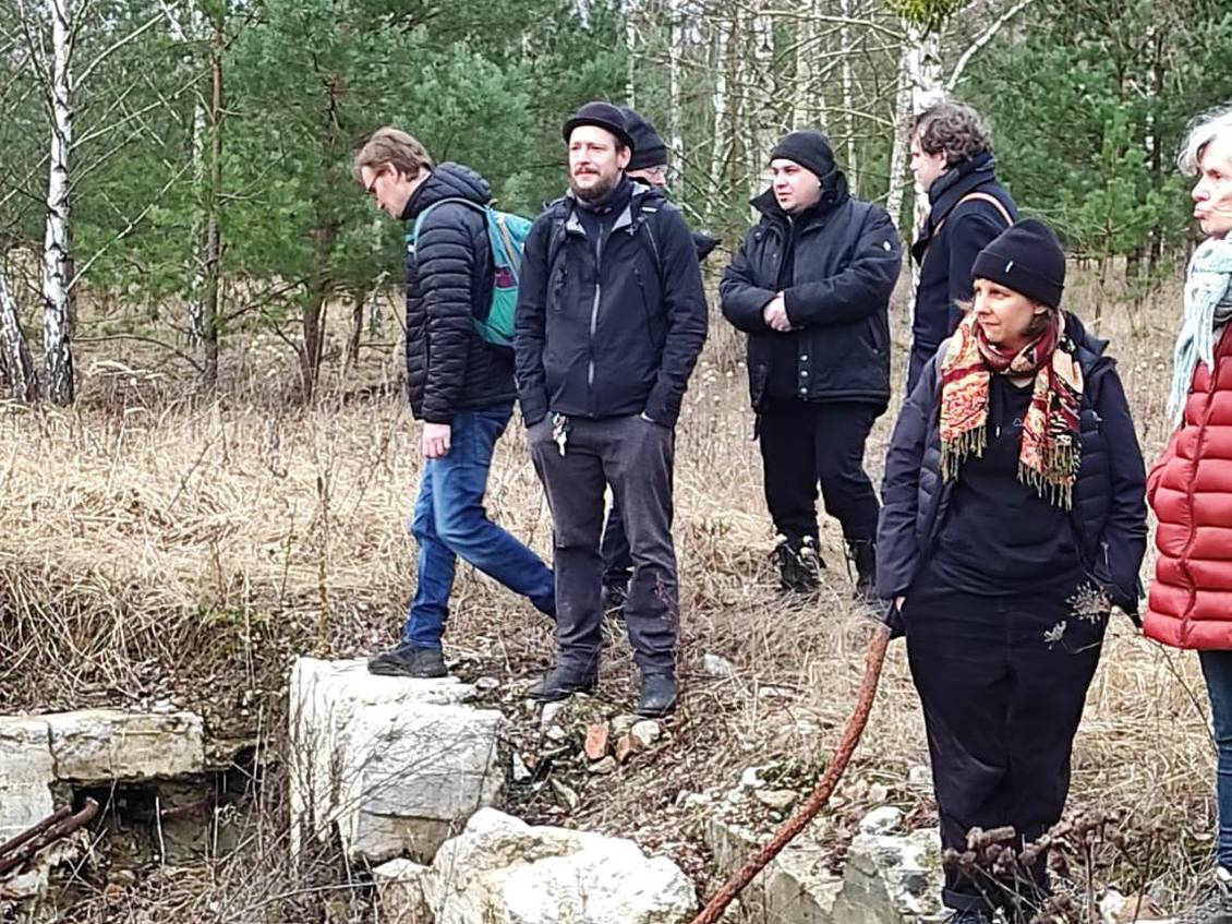Das Foto zeigt eine Gruppe von Menschen vor Ruinen in einem Wald.
